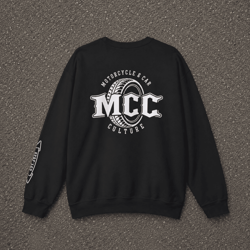 A black crewneck sweatshirt laid flat on a textured gray asphalt surface, featuring a large white graphic on the back with the text 'MCC Motorcycle & Car Culture' and a tire design, plus a smaller white graphic on the left sleeve.