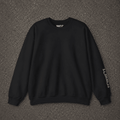 A black crewneck sweatshirt with white graphic text on the inner neck and left sleeve, laid flat on a dark gray asphalt background.