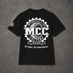 A black short-sleeve t-shirt laid flat on a textured gray background, featuring a large white graphic print on the back with the text 'MCC Motorcycle & Car Culture Est. 2026' and 'No Cages.