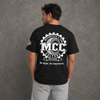 A man viewed from behind wearing a black t-shirt with a large white graphic on the back that reads 'MCC Motorcycle & Car Culture Est. 2026' and 'No Cages. No Compromises.