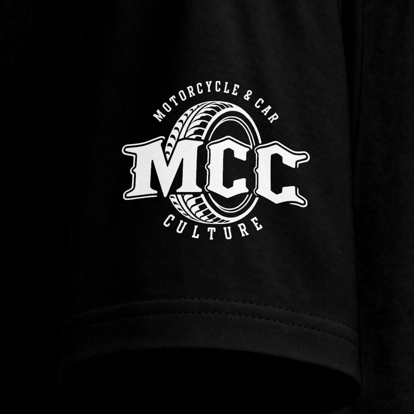 Close-up of a black short-sleeve T-shirt sleeve with a white circular graphic on the upper arm reading 'MCC Motorcycle & Car Culture' around a tire design.