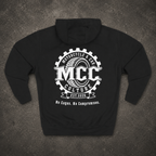 A black pullover hoodie shown from the back, laid flat on a dark textured surface. The back features a large white circular graphic with a tire and gear design, reading 'MCC Motorcycle & Car Culture' and 'No Cages. No Compromises.