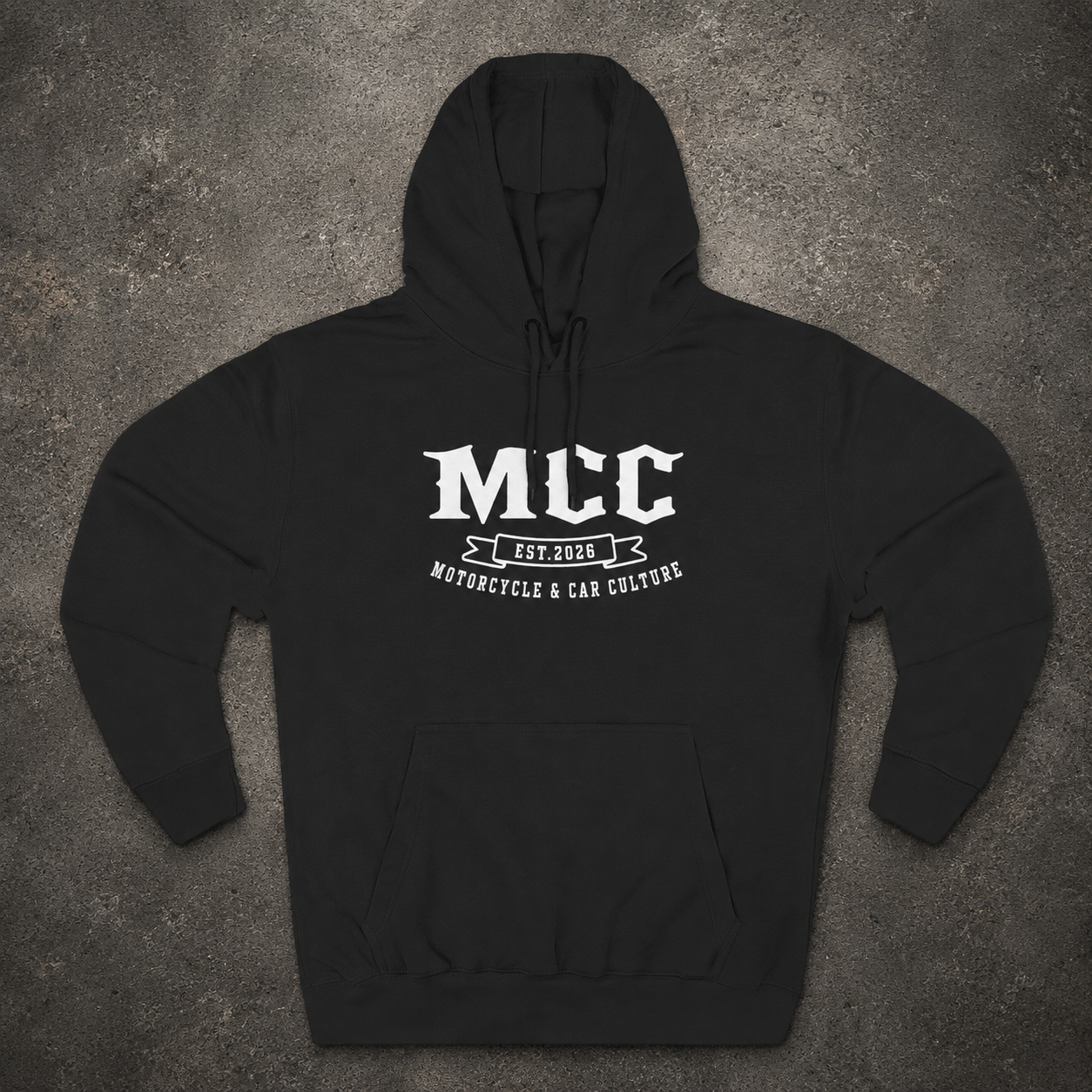 A black pullover hoodie laid flat on a textured gray background, featuring a white graphic print on the chest that reads 'MCC' with 'EST. 2026' and 'MONORCYCLE & CAR CULTURE' below.