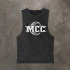 A dark gray Stonewashed sleeveless tank top featuring a white graphic print of the letters 'MCC' inside a tire design, laid flat on a textured gray concrete background.