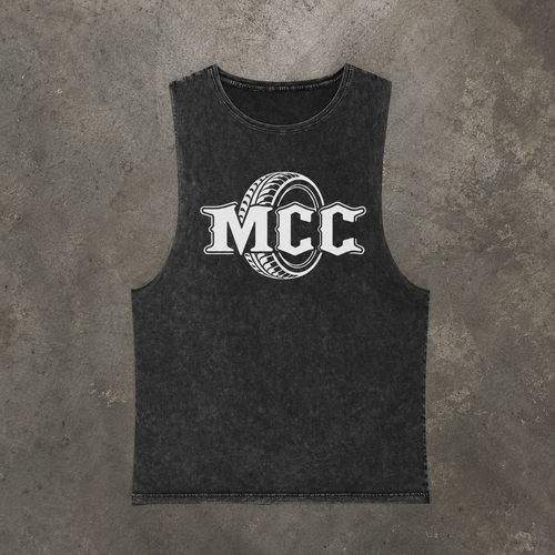 A dark gray Stonewashed sleeveless tank top featuring a white graphic print of the letters 'MCC' inside a tire design, laid flat on a textured gray concrete background.