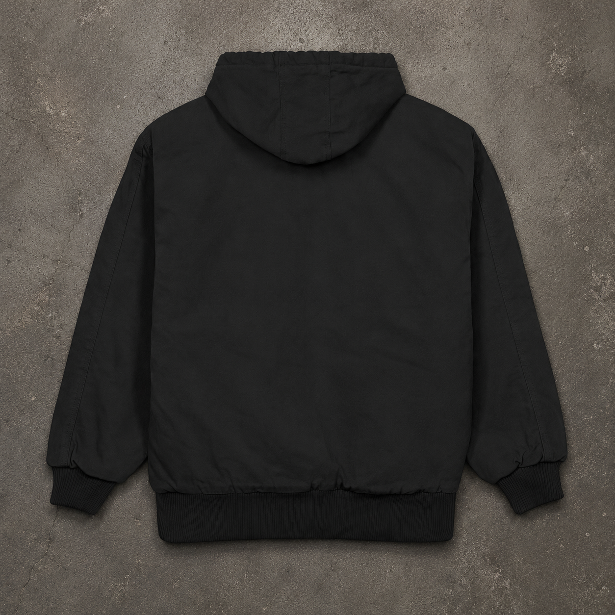 A black hooded jacket shown from the back, laid flat on a textured gray concrete surface.