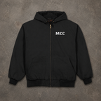 A black zip-up hooded jacket with 'MCC' printed in white on the left chest, laid flat on a textured gray concrete background.